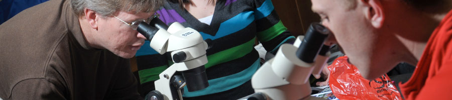 Dr. Mark Bolyard looks through the microscope with his students in lab.