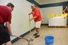 Hunter Baker (left), associate dean of arts and sciences, and Tim Ellsworth, director of news and media relations, scrape wax from the cafeteria floor at Lloyd Wood Middle School in preparation for Holt elementary students. Water damage from devastating tornadoes closed Holt elementary, forcing the school to move into the vacant Lloyd Wood school in Northport, Ala. - Photo by Beth Spain