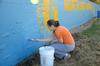 Kaitlin Watson, sophomore nursing major,  paints the football field wall at North Side High School as part of a community service project on Campus and Community Day.  - Photo by Ebbie Davis