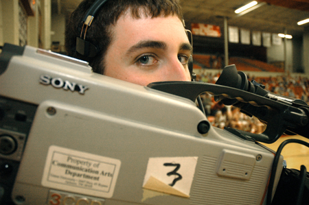 Aaron Hardin peeks over his camera while filming a basketball game.