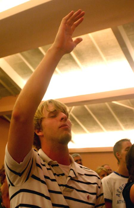 Sophomore Carter Collins raises his hand in praise as he sings along during the family chapel on the first day of orienation.