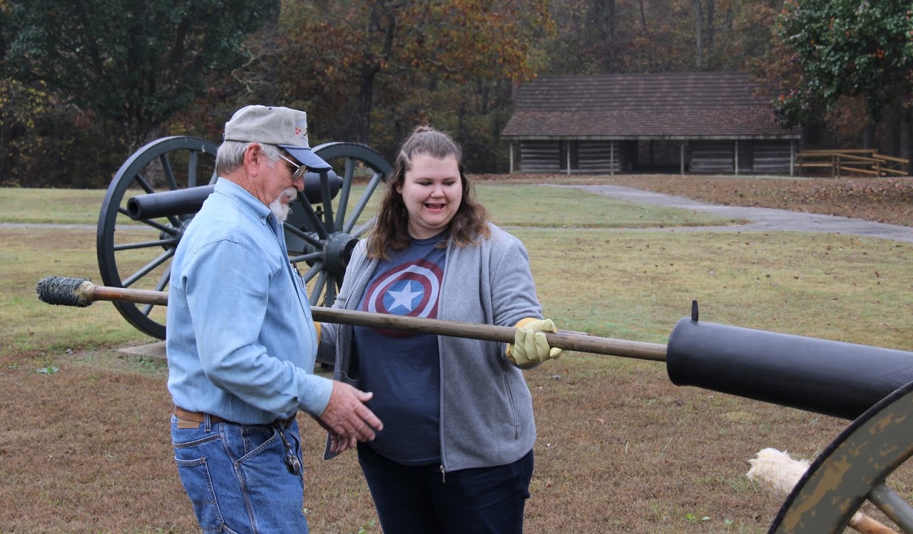 Britton Lane Battlefield Association President Jim Weaver explains to Jessica Barton what to do as she uses a rammer to push a gunpowder packet down the barrel of a cannon on November 3, 2015.