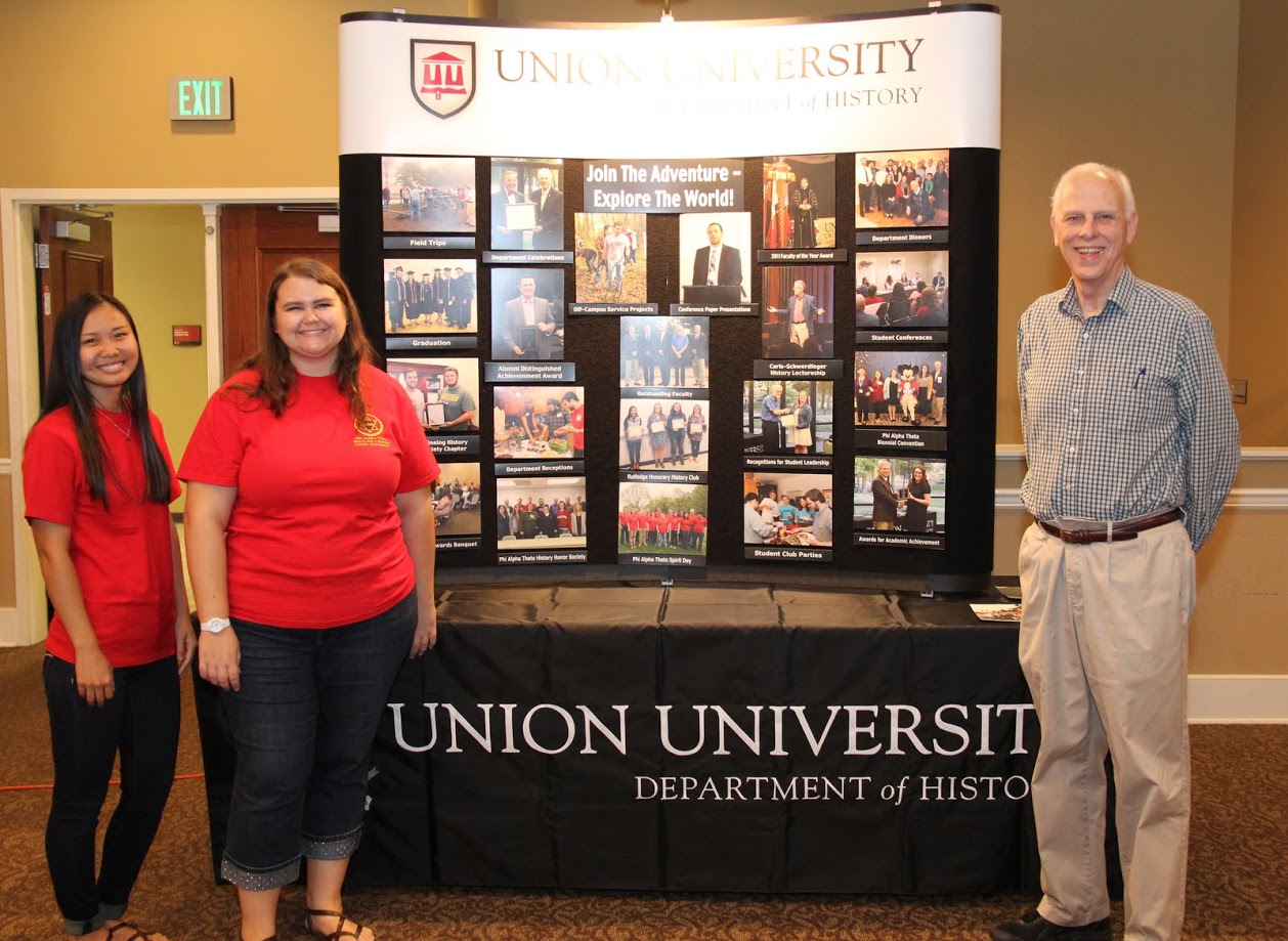 Phi Alpha Theta members Katherine Cheshire (left) and Jessica Barton stand with Dr. Stephen Carls by the history display at the Big Top Campus Life Fair on August 20, 2017.