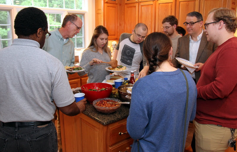 Attendees at the Phi Alpha Theta cookout on May 11, 2019, go through the food line at Dr. Stephen Carls's home. They are (going clockwise, starting on the left) Tracy Newsome (back to camera), Robert Briley, Addison Osborne, Will Choate, Luke Sower, Dr. Keith Bates, Nathan Heatherly, and Katie Allison (back to camera).