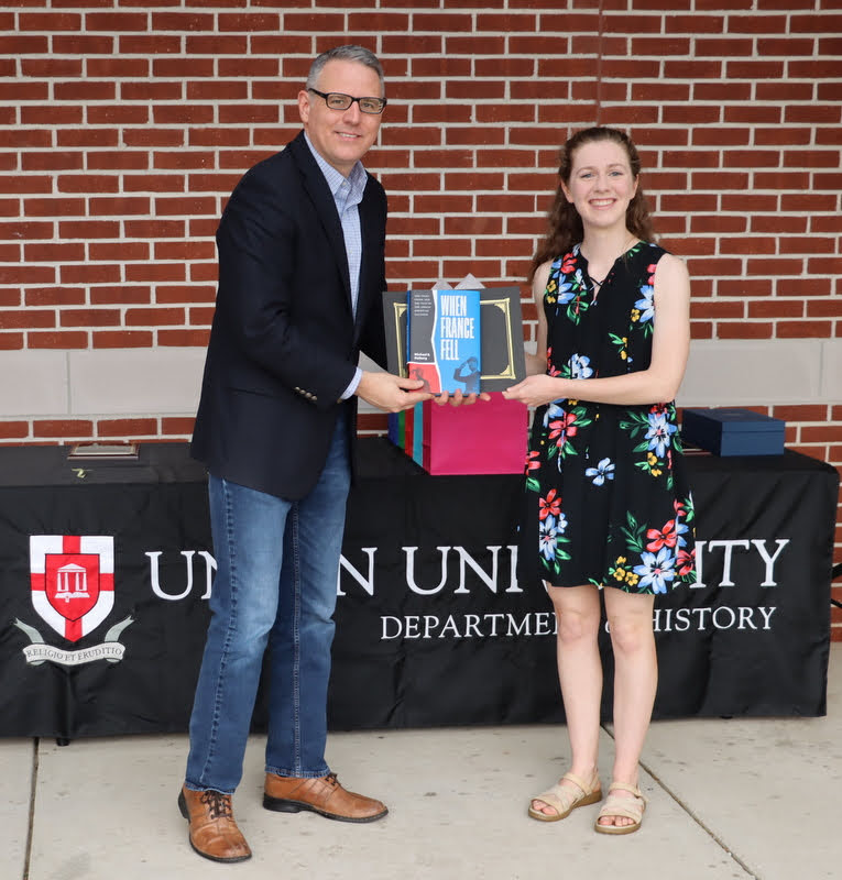 Anne Adams receives a book and certificate of recognition from Dr. Keith Bates at the History Department Awards Program on April 28, 2022, for the excellent paper she presented at the Arkansas Phi Alpha Theta Regional Conference on April 2, 2022.