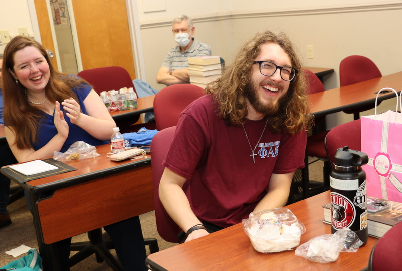 Delta-Psi chapter member Nicholas Palmer (front right) expresses joy after receiving birthday greetings and a birthday cupcake from the chapter at the Phi Alpha Theta spring plenary meeting on February 20, 2023. Behind him are Abigail Gilbert and Dr. Terry Lindley (back right).