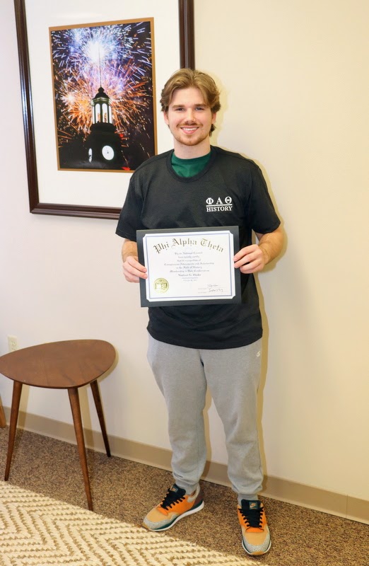 New Delta-Psi chapter member Nathan Hicks holds his Phi Alpha Theta membership certificate and wears his Phi Alpha Theta T-shirt on February 28, 2023.