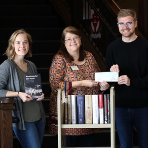 Delta-Psi Chapter President Luke Sower (second from right) presents a Phi Alpha Theta Best Chapter Award check for $250 to Library Director Melissa Moore on December 5, 2019. Chapter Vice President Megan Ledbetter (left) and Dr. Stephen Carls (right) each hold one of the history books that the chapter purchased with the prize money. The other purchased books are on the book cart. Photo by Kristi Woody