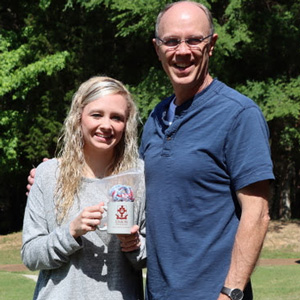Graduating Phi Alpha Theta member Jennifer Briley holds her history department coffee mug and PAT honor cord while standing with her father, Robert Briley, during a presentation ceremony at Dr. Stephen Carls's home in May 2020.