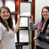 Delta-Psi President Jordan Sellers (left) and Vice President Kathryn Mitchell hold the 2016 Phi Alpha Theta Best Chapter Award certificate in front of the spot where it will be placed in the history department's display case. The certificate arrived in the mail on September 26, 2016.
