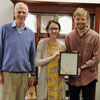 Dr. Stephen Carls (left to right), Delta-Psi Chapter President Lauren Butler, and Vice President Luke Sower stand with the 16th straight Phi Alpha Theta Best Chapter Award that the group received in the mail on October 18, 2018. Behind them is a history display case containing many of the chapter's previous Best Chapter Awards.