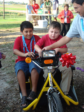 Armando Sanchez (center) gets some help with his new electronic tricycle from his brother Jose (left) and his father Victor.

