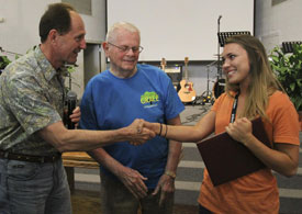 Art Rorheim (center), co-founder of Awana, and Jack Eggar, president and CEO of the ministry, surprise Lindsey Blackwood, media communications major, with her degree May 17 at the Louisiana State Penitentiary in Angola, La. (Photo by Brittney Julian)