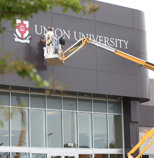 Workers change the lettering at the Union University building on Emporium Drive to reflect the new School of Adult and Professional Studies. (Photo by Kristi Woody)