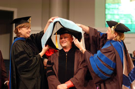 Provost Carla Sanderson (left) and Dr. Michelle Atkins (right), director of graduate studies in education, place the doctoral hood over the head of Mike Bevis, principal of East Intermediate School, during Union University's August graduation ceremony at West Jackson Baptist Church.