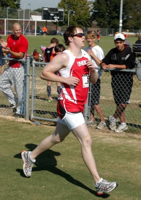 Grant Luke crosses the finish line during the Union University Cross Country Invitational.  Luke, also a member of the Union baseball team, receives applause from one of his teammates, Kevin Kirksey. - Photo by Steven Aldridge