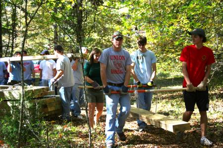 Amy Brown, junior Biblical studies major, David Conway, freshman history major, Chad Keathley, junior theology major, and Noah Arnold, junior history major, form a foursome to carry a heavy cedar plank to a drop-off point along the walking trail under construction at Pinson Mounds during Day of Remembrance. - Photo by Kristi McMurry Woody