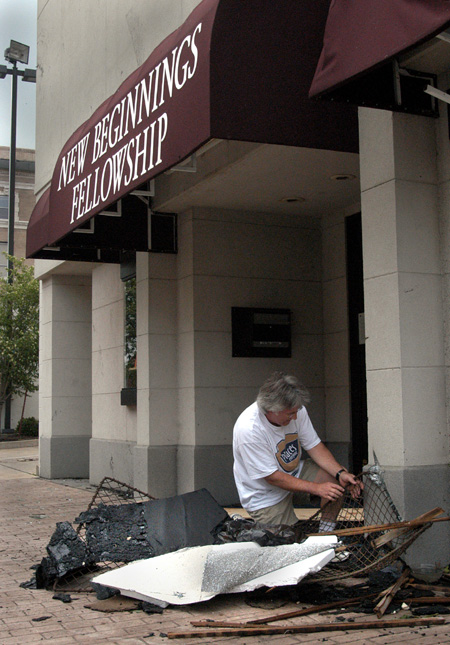 Union theatre professor and New Beginnings Fellowship elder David Burke tries to work loose a chainlink gate which was hurled into the church's exterior wall by the winds of the tornado. - Photo by Jim Veneman
