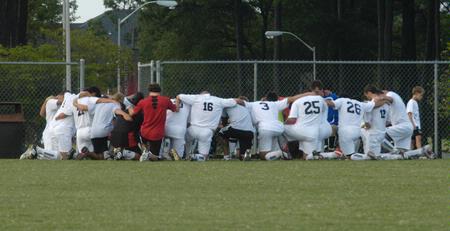 The soccer team kneels in prayer for Kevin Bradley, Senior, who was injured on the field during the men's soccer game against Reinhardt College on Sept. 12 - Photo by Sarah Palmer Goff
