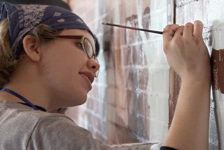 Kelsey Roberts, senior painting major, adds detail to the faces on the mural at Daddy's Kitchen Table Soup Kitchen on Campus and Community Day. - Photo by Megan Bailey