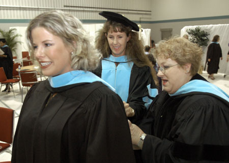 Germantown adjunct education professors Dr. Pam Curry (center) and Dr. Bess Anne McKnight (right) assists Master of Education graduate Jacquelyn Threlkeld (left) with her hood shortly before the August 2003 commencement exercises. - Photo by Jim Veneman