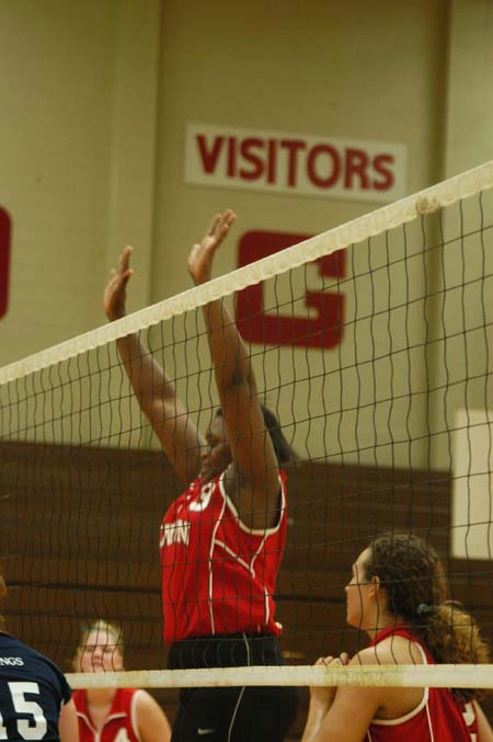 Phylis Anyango (13) goes up for a block.  Lindsay Stahlberg (4) and Crystal Abel (12) stand and wait. - Photo by Steven Aldridge