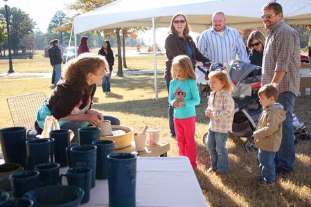 Rachel Moore, junior art major, works on her potter's wheel as homecoming visitors stop by for a chat. Moore was among several artists and students displaying and demonstrating their work at Arts in the Park.  - Photo by Ebbie Davis