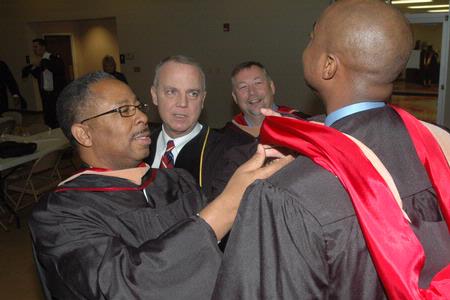 Michael Gray, MBA graduate, along with Dr. Bill Nance, associate dean of McAfee School of Business Administration, help Stacey Miller prepare for the graduation ceremony at West Jackson Baptist Church. - Photo by Beth Spain