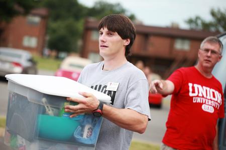 Georg Pingen, assistant professor of engineering, carries a new student's belongings to her room during New Student Move-in.  - Photo by Kristi McMurry Woody
