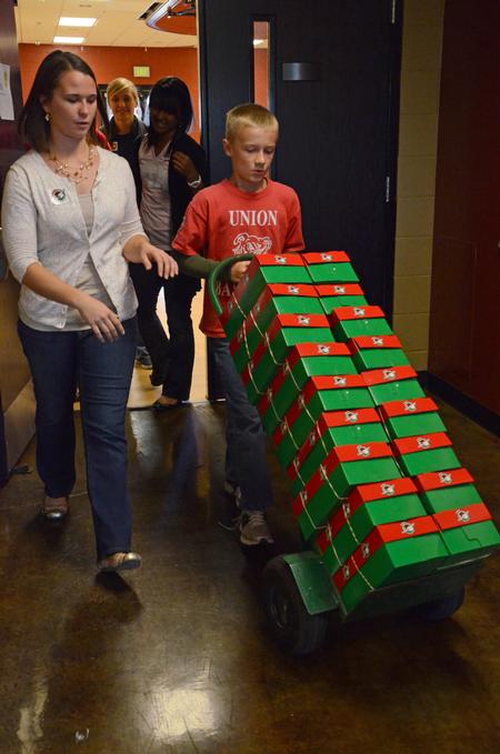 Jodie Gardner, junior nursing major, walks alongside Nate Barnard as they wheel out the Operation Christmas Child boxes that were packed on Campus and Community Day.  - Photo by Anne Richoux