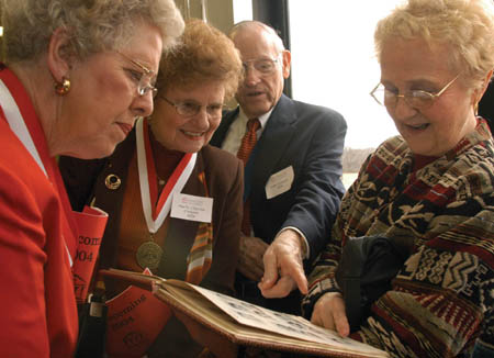 Sue Crocker (’54), Paula Clayton (’54), Fred Cosson (’50), and Christine Fairless (’51) look through the 1954 yearbook during the Class of '54 Reunion Luncheon at Homecoming 2004. - Photo by Jim Veneman