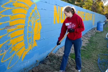 Christa Seyler, freshman nursing major, clears away grass on the football field at North Side high school, in order to re-paint the wall. - Photo by Ebbie Davis