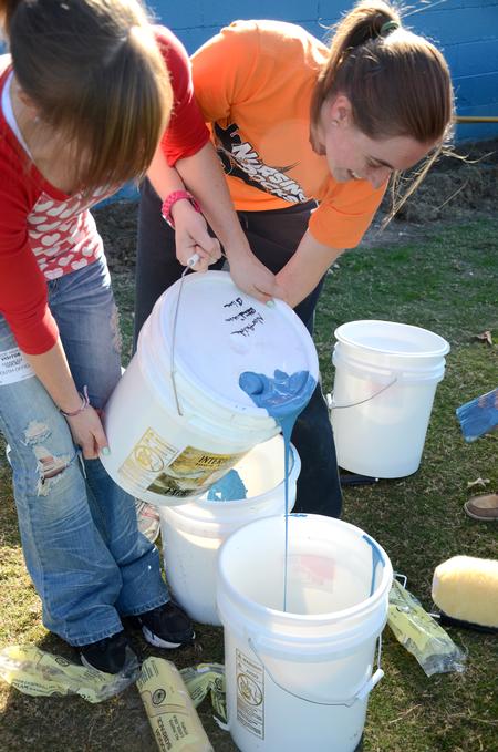 Hannah Gerling, freshman nursing major and Beth Murphy, sophomore nursing major and team leader, pour the paint for the wall by the football field at North Side High School. - Photo by Ebbie Davis