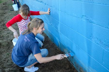 Freshmen nursing majors, Hannah Gerling and Rachel Massey, paint the wall on North Side High School's football field during Campus and Community Day.  - Photo by Ebbie Davis