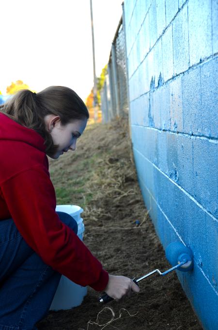 Christa Seyler, freshman nursing major, paints the football field wall at North Side High School during Campus and Community Day. - Photo by Ebbie Davis