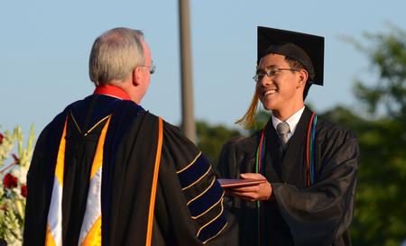 David S. Dockery, president of the university, presents biology major David Koh with a diploma during spring graduation. - Photo by Jacob Moore