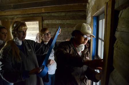 Glenae Nora, senior history major, applies painter's tape around the window frame of a historic cabin at Parker's Crossroads Battlefield. Members of the history department whitewashed the walls during the tenth annual Campus and Community Day. - Photo by Jacob Moore