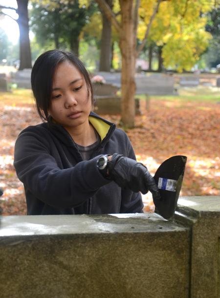 Katherine Cheshire, freshman history major, removes moss from a tombstone at Jackson's historic Hollywood Cemetery during Campus and Community Day. - Photo by Jacob Moore