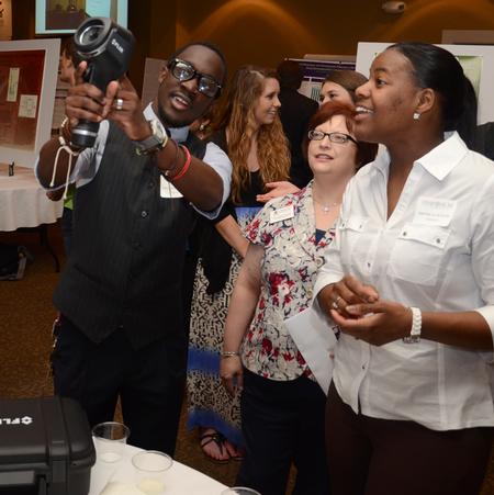 Jeremiah Murila, sophomore engineering major, demonstrates how to use a thermal imaging camera to assistant registrar Nita Pearce and Monica Austin, senior chemistry major, during the annual Scholarship Symposium. - Photo by Jacob Moore