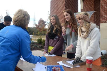 Candace Ridley, junior exercise science major, Sunni Duffey, junior pharmacy major, and Zoe Sudbury, junior exercise science major, help runners check in at Chi Omega's Make-a-Wish 5K during homecoming. - Photo by Meg Rushing