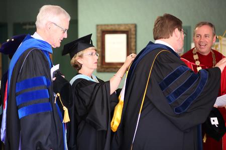 Cheryl Mercker, administrative assistant to the senior VP for business services, adjusts C. Ben Mitchell's hood before the processional into Awards Day chapel. - Photo by Kristi McMurry Woody