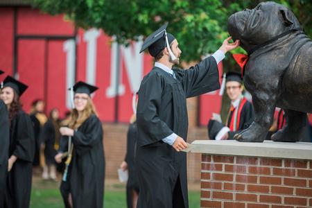 Chris Hare, digital media studies graduate, scratches the chin of the Buster the Bulldog statue as he walks toward the Great Lawn for spring commencement services.  - Photo by Kristi McMurry Woody