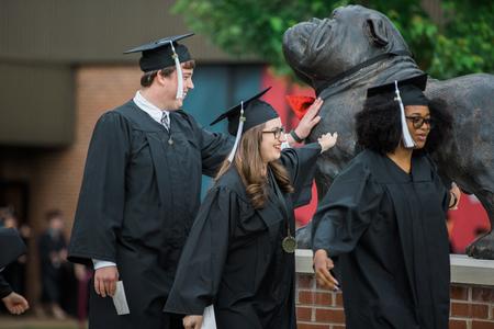 Graduates Brady Teague, Danica Smithwick and Nyree Smith pass by the Buster the Bulldog statue on their way to the Great Lawn for spring commencement services.  - Photo by Kristi McMurry Woody