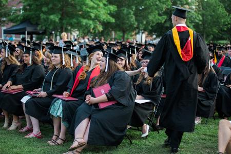 Kelsie Edgren, English graduate, high fives her husband Joshua, physics with honors graduate, as he is walking back to his seat after receiving his diploma at spring commencement services.  - Photo by Kristi McMurry Woody