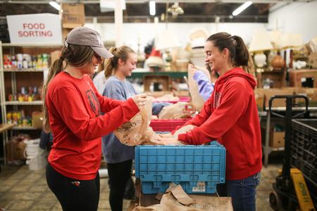 Austen Deloach, business administration major, and Julie Stauffer, head assistant coach for the women's soccer team, help pack up bags for the RIFA snack backpack program during Campus & Community Day. - Photo by Kristi McMurry Woody