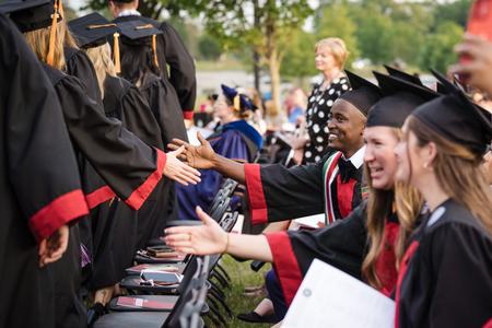 Collins Kimutai Koech, Nursing major from Eldoret, Kenya, congratulates graduates as they leave their seats to receive their diplomas at Spring Graduation. - Photo by Kristi McMurry Woody