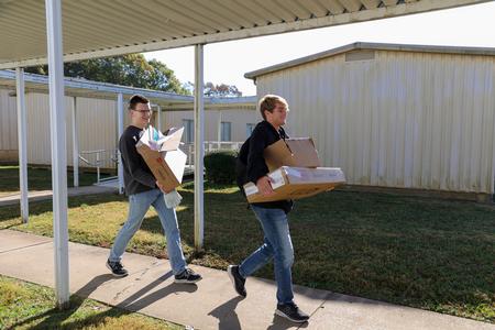 Timothy White and Riley Garrison carry boxes of furniture to assemble for Nova Early Learning Center on Campus and Community Day. - Photo by Karley Hathcock