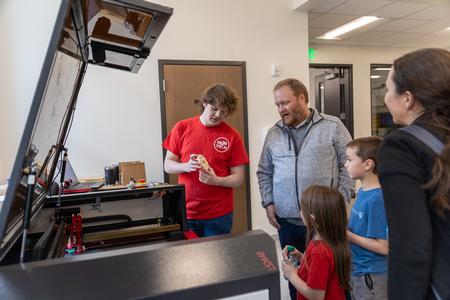 A Hub Tech shows a family how the laser cutter works in The HUB at The Ethos Forum during the building's dedication. - Photo by Jim Gandy