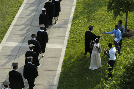 Graduates file onto the Great Lawn at the beginning of the graduation ceremony while one graduate jumps out to say hello to a friend. - Photo by Kathleen Murray