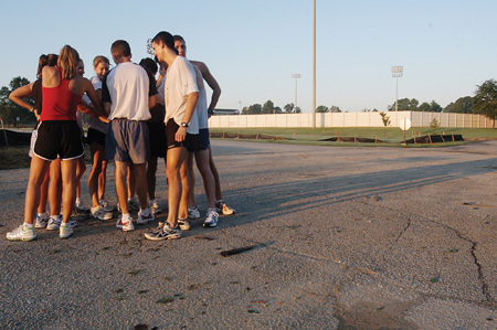 The cross country teams gather together for a quick prayer in the parking lot as the sun rises following the teams second early-moring practice of the season. - Photo by Brad Moore